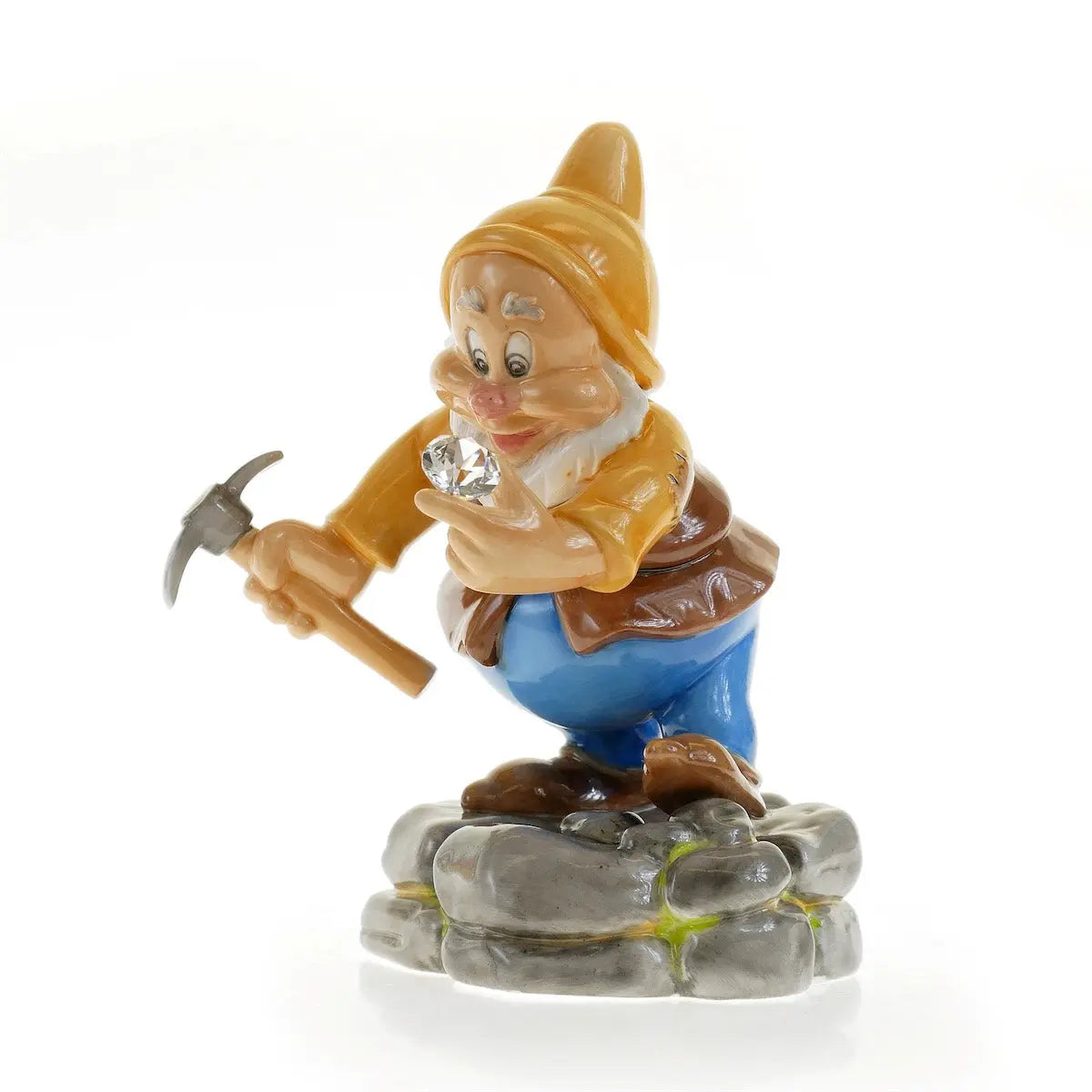 Happy dwarf figurine in yellow hat and brown tunic, holding a pickaxe on grey rocks