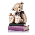 Sitting teddy bear figurine with brown fur, dark bowtie, and book stack with purple trim